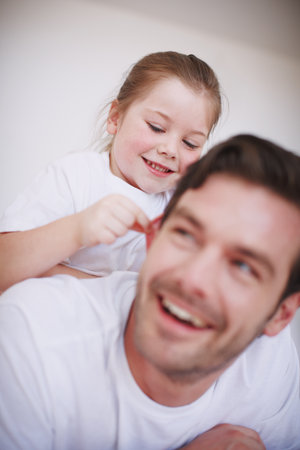She loves to play with her Dad. a little girl sitting on her fathers back and being playful.の写真素材