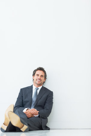 Smart smiling executive sitting against wall. Portrait of smart male executive sitting against wall and giving you an attractive smile.の写真素材