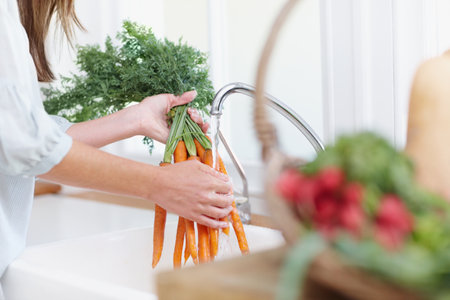 Nice and clean. Closeup of a woman washing carrots in the kitchen sink.の写真素材