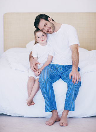 Essential bonding time with his little girl. Portrait of a dad and his young daughter sitting side by side on a bed.の写真素材