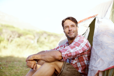 Watching the nature around him. A handsome young man sitting at the entrance to his tent.の写真素材