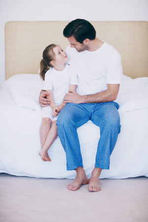 I love you my little angel. A loving father and daughter sitting next to each other on a bed.の写真素材