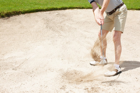Hoping this shot was enough...Senior man trying to hit his ball out of the sandtrap on the golf course.の写真素材