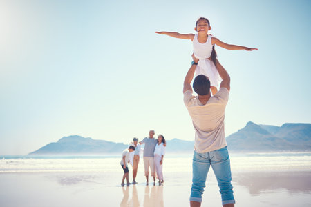 Beach, family and girl with father, airplane and playing, happy and carefree against blue sky background. Freedom, flying and child with parent, grandparents and sibling on ocean travel or holidayの写真素材
