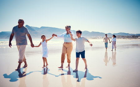 Beach, family holding hands and grandparents with children playing and walking on ocean sand together. Fun, vacation and senior man and woman with kids bonding, quality time and summer walk in natureの写真素材