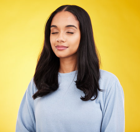 Indian woman with eyes closed, meditation and zen with peace and calm isolated on yellow studio background. Mental health, wellness and balance with stress relief, young female relax with mindfulnessの写真素材