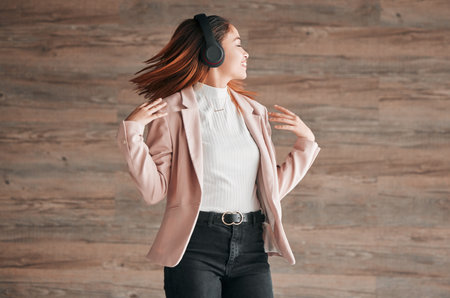 Dancing, happy and woman listening to music with happiness or streaming audio online using headphones. Radio, wellness and excited female person dance isolated in a wooden wall backgroundの写真素材