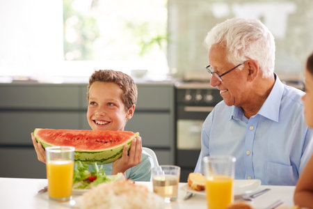 Bet you I can it all of this. a little boy holding a large slice of watermelon while his family look on.の写真素材