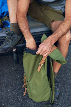 Making sure everythings packed. a man sitting in the back of his vehicle with a backpack.