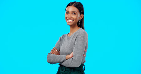 Face, smile and business woman with arms crossed in studio isolated on a blue background. Boss, professional and happy, funny and confident female entrepreneur from India with pride for career or jobの写真素材