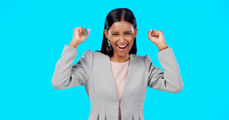 Yes, winning and woman cheers isolated on blue background celebration, excited and fist pump for lotto. Wow, happy winner or indian person face to celebrate prize, competition or bonus news in studioの写真素材