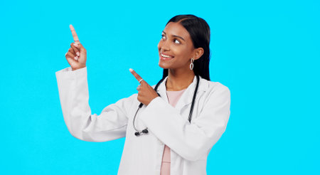 Healthcare doctor, studio and happy woman point at medical promotion, hospital notification or clinic announcement mockup. Nurse portrait, advertising surgeon and marketing person on blue backgroundの写真素材