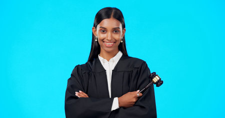 Lawyer, face and happy woman with gavel in studio, blue background and color backdrop. Portrait, female judge and legal attorney with arms crossed, smile and confidence for justice of constitutionの写真素材