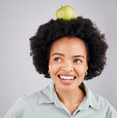 Thinking, apple on head and black woman with smile, health and nutrition against a grey studio background. African American female, fruit and happy lady with happiness, diet and wellness with ideasの写真素材