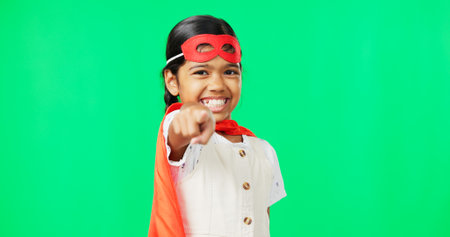 Superhero, point and face of child on green screen for fantasy, cosplay costume and comic character. Choose gesture, hero mockup and portrait of girl in studio for freedom, fight crime and gamesの写真素材