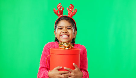 Christmas, gift box and happy with girl in green screen studio for youth, celebration and festive. Present, cheerful and vacation with portrait of child on background for season, holiday or happinessの写真素材