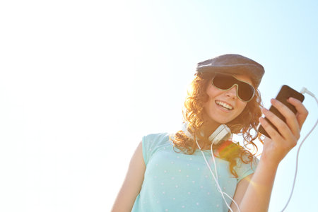 Creating the perfect summer playlist. A redheaded adolescent girl selecting a playlist on her smartphone while standing outside.の写真素材