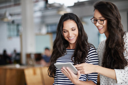 Technology makes everything easier. Two female colleagues posing together in their creative work space.の写真素材