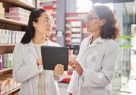 Pharmacy, tablet and stock with women in a dispensary talking about prescription medicine for an online order. Healthcare, technology or diversity with a female pharmacist team working in a drugstoreの写真素材