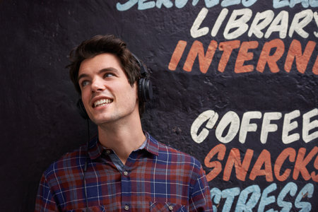 Music will hit you but it wont hurt. a young man standing against a wall listening to music.の写真素材
