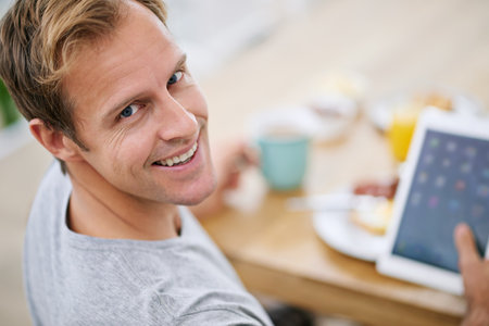 Relaxing on his day off. Portrait of a handsome man using his tablet while having breakfast at home.の写真素材