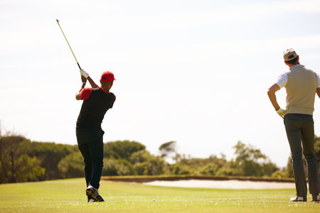 Its all in the swing. two handsome men playing a game of golf.の写真素材