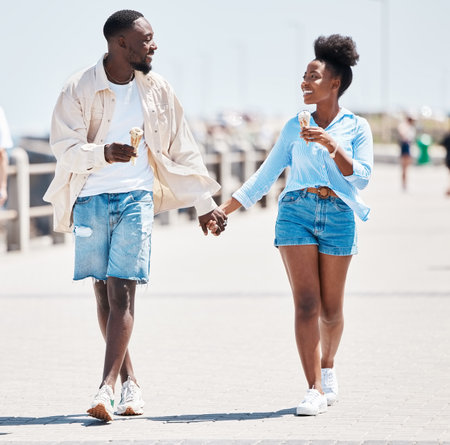 Couple ice cream, promenade summer walking and love, relax and carefree fun together outdoors. Young black people holding hands, smile partners on a date and happy romantic relationship on sunny dayの写真素材