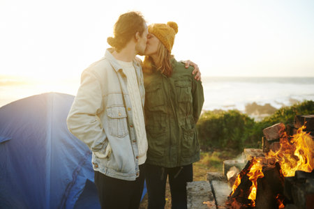 Getting their camp warmed up. an affectionate young couple getting warm by the fire.の写真素材