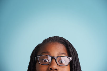 Taking a peek. Cropped portrait of a young boy wearing glasses against a blue background.の写真素材
