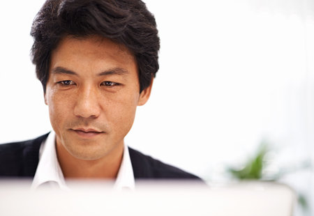 Focussed on the job at hand. a handsome asian businessman working on his laptop in the office.の写真素材