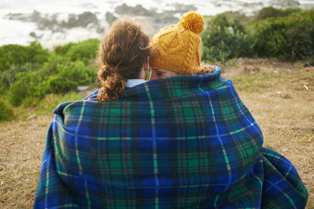 Snuggling up with a loved one. Rearview shot of an affectionate young couple wrapped in a blanket at...