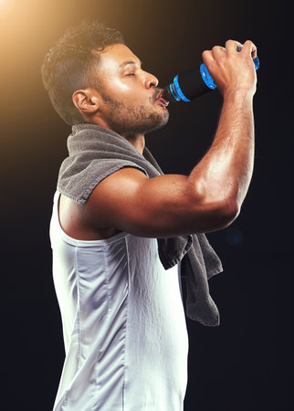 Rehydrating after an epic workout. Studio shot of a fit young man isolated on black.の写真素材