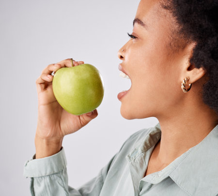 Apple, health and black woman in studio eating for nutrition, wellness and healthy snack. Food, diet and face profile of girl eat green fruit for detox, vitamins and weight loss on white backgroundの写真素材