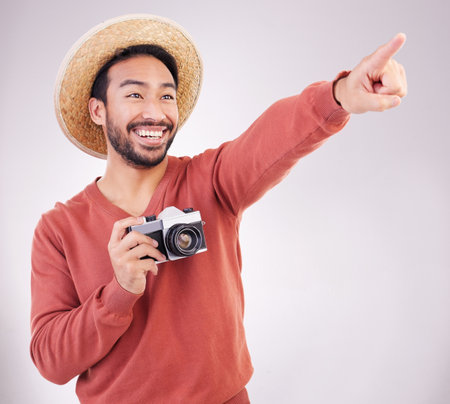 Travel, camera and excited man pointing at view in studio on holiday with adventure, fun and white background. Smile, discovery and happy tourist on vacation, photographer on journey with happiness.の写真素材