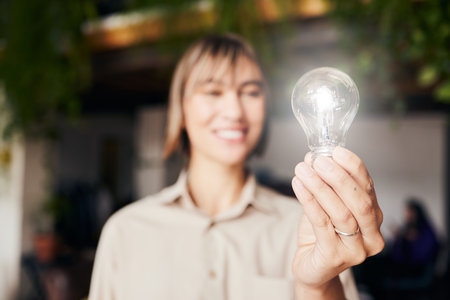 Lightbulb, happy and a woman with light from inspiration, knowledge or ideas at work. Smile, innovation and an employee with power, creativity and energy at a company with optimism and visionの写真素材