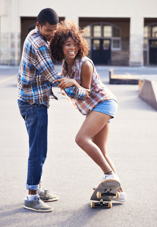 Youll get the hang of it. a young man teaching his girlfriend how to skateboard.の写真素材
