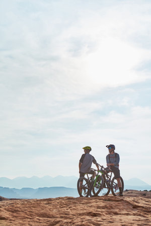 The best days are spent on a mountain bike. Full length shot of two athletic men taking a break to admire the view while mountain biking through the wilderness.の写真素材