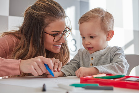 Hes only starting to learn how to hold and use crayons. a woman and her young son using crayons to draw at home.の写真素材