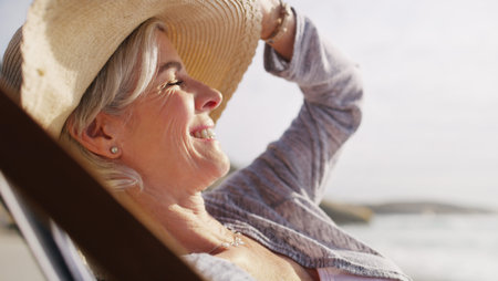 I havent enjoyed a beach day like this in a while. an attractive senior woman relaxing on a lounger...