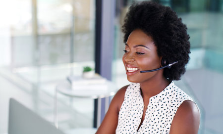 Service with a smile. a call centre agent smiling at her desk.の写真素材
