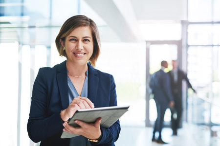Work smart and you can guarantee success. an attractive young businesswoman using a digital tablet in an office with her colleagues in the background.の写真素材