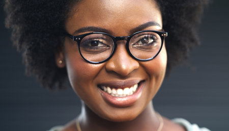My new glasses is the reason for my smile. a happy young woman posing against a dark background.の写真素材