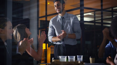 We can do this together. a diverse group of businesspeople clapping after a successful meeting in the office late at night.の写真素材