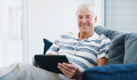 Connect to the comfortable life. a senior man using a digital tablet on the sofa at home.の写真素材
