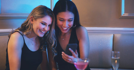 Oooh, we look good. two young women using a smartphone together in a nightclub.の写真素材