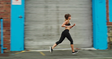 Training for my next marathon. Full length shot of an attractive young woman wearing gym wear and running down the street alone.の写真素材