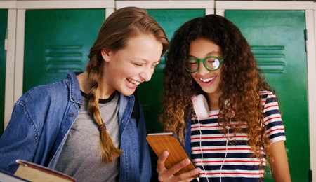 I cant believe he messaged you back. two young school kids browsing on a cellphone together while waiting to go to class inside of a school.の写真素材