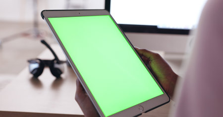 Close up of an African American persons hands holding a tablet with a plain green screen with a blurred background of headphones. Technician working out how to fix broken device. IT problem solvingの写真素材