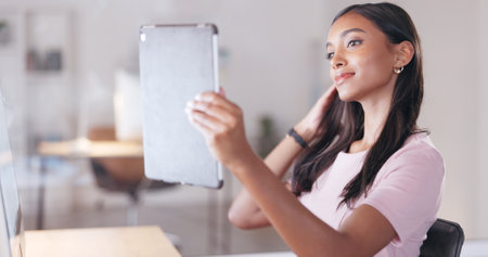 Young happy woman taking a selfie with a digital tablet while relaxing in an office at work. One smiling female student taking pictures to post on social media while sitting alone in a libraryの写真素材