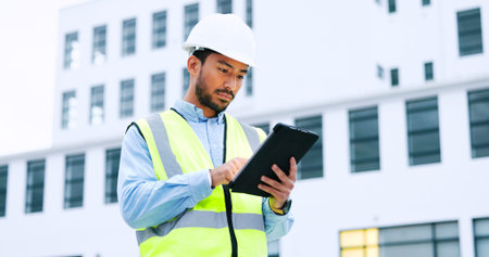 Male engineer checking data on digital tablet and inspecting construction site. Technician in a hardhat doing management and project planning outdoors. Skilled worker looking or overseeing operationsの写真素材